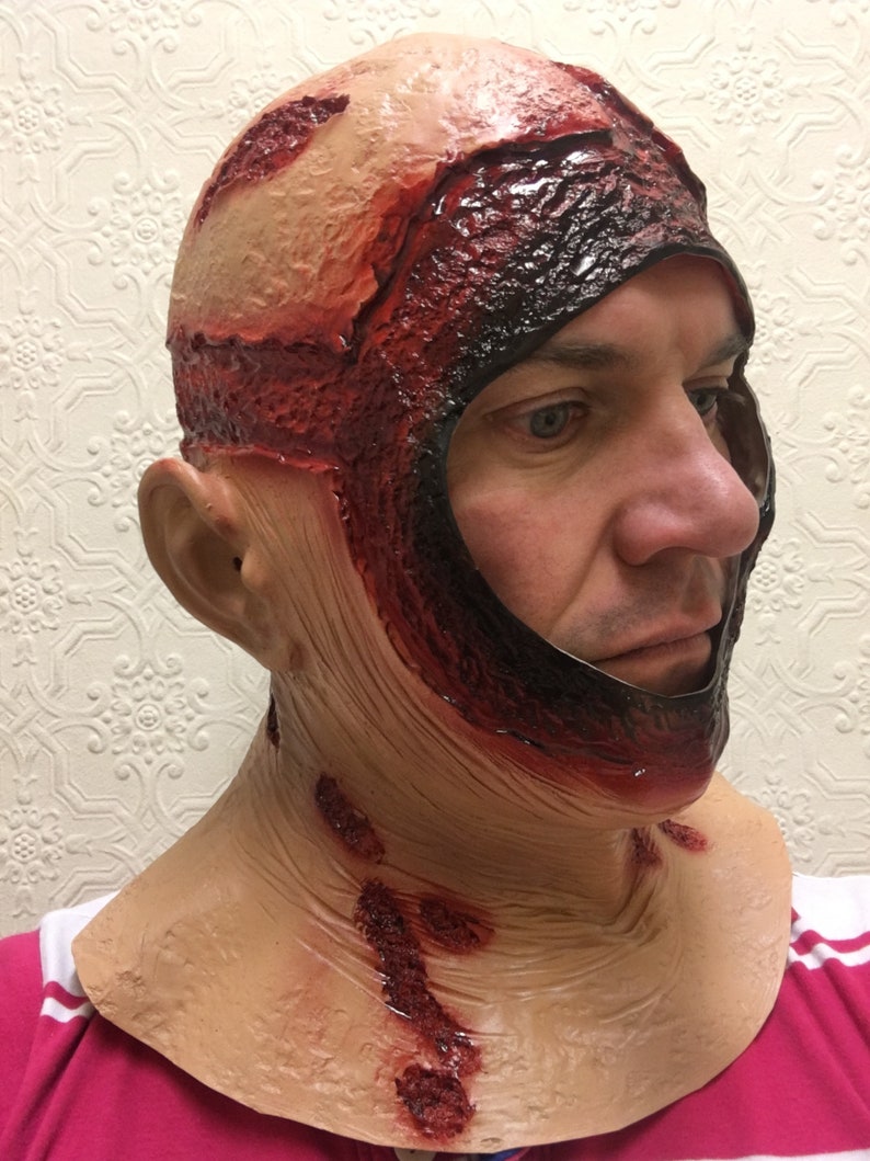 Może przedstawiać: Lateksowa maska ​​na Halloween przedstawiająca makabryczną, odsłoniętą sk&oacute;rę głowy i twarz. Maska ma realistyczne detale, z obszarami rozdartej sk&oacute;ry, odsłoniętym mięsem i symulowaną krwią. Maska zakrywa głowę i szyję.