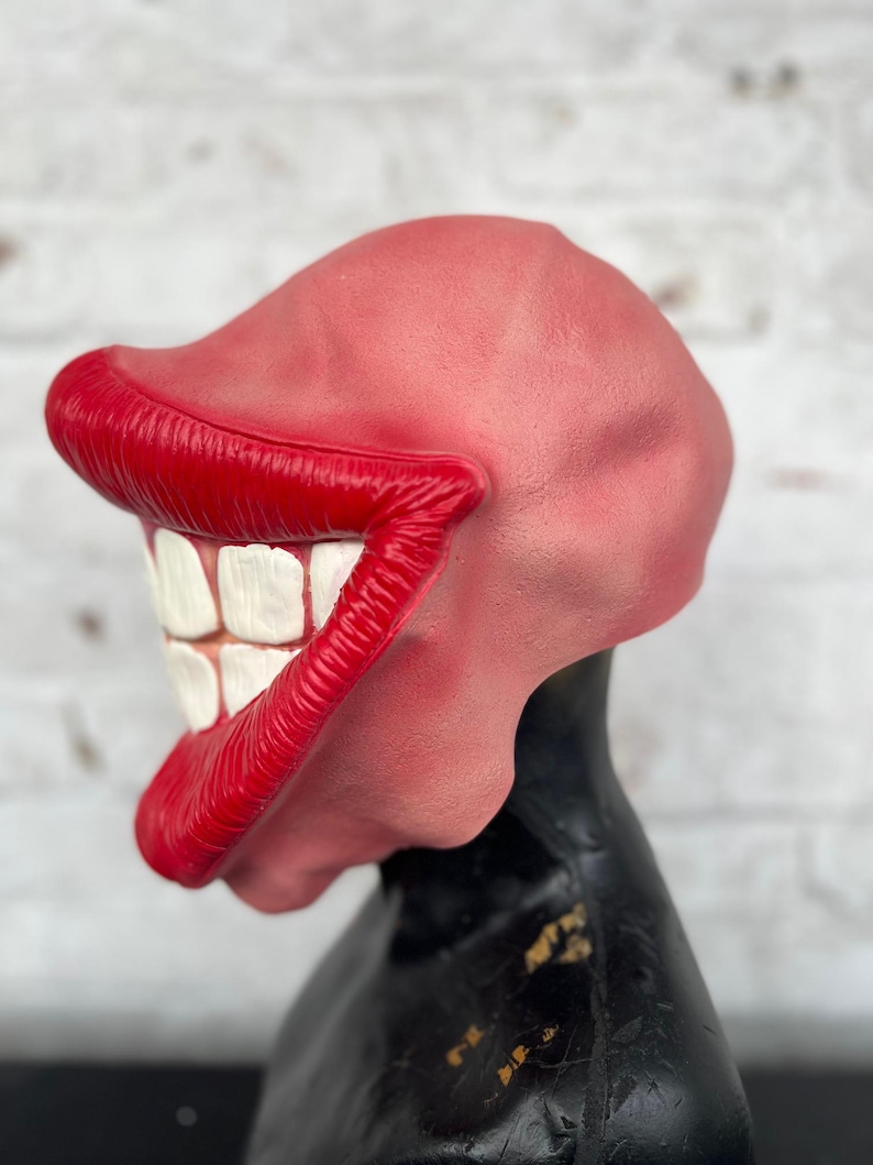 Puede incluir: Una m&aacute;scara de pl&aacute;stico roja y blanca con una gran sonrisa exagerada. La m&aacute;scara tiene labios rojos y dientes blancos.