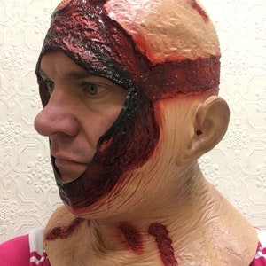 Może przedstawiać: Lateksowa maska ​​na Halloween przedstawiająca realistyczną, odsłoniętą sk&oacute;rę głowy ze szczeg&oacute;łowymi efektami krwi i mięsa. Maska zakrywa głowę i szyję, z podartym wyglądem i symulowanymi ranami. Kolorystyka obejmuje odcienie czerwieni, beżu i czerni.