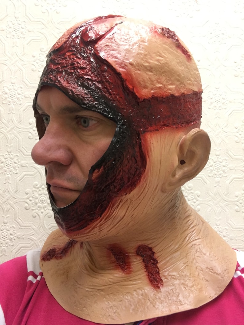 Może przedstawiać: Lateksowa maska ​​na Halloween przedstawiająca realistyczną, odsłoniętą sk&oacute;rę głowy ze szczeg&oacute;łowymi efektami krwi i mięsa. Maska zakrywa głowę i szyję, z podartym wyglądem i symulowanymi ranami. Kolorystyka obejmuje odcienie czerwieni, beżu i czerni.