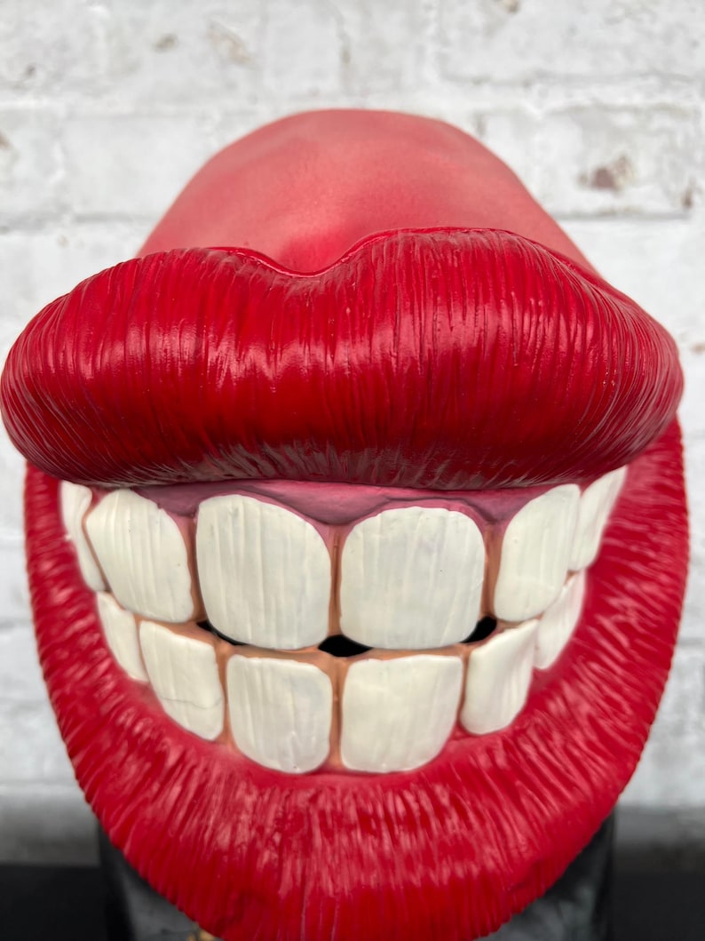 Puede incluir: Una m&aacute;scara de pl&aacute;stico roja con una gran sonrisa de dientes y labios rojos brillantes. La m&aacute;scara est&aacute; dise&ntilde;ada para parecer una boca gigante.