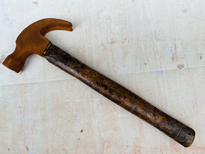 Pu&ograve; includere: Un martello marrone arrugginito con un manico di legno. Il martello ha una testa di metallo con un artiglio sul retro.