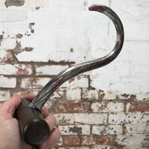 May include: A silver metal hook with a wooden handle. The hook is curved and has a red stripe running along the length of the hook.