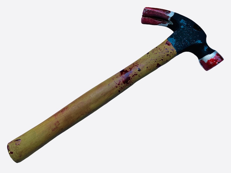 May include: A yellow wooden handled hammer with red and black paint splattered on it. The hammer head is black with red paint on the claw and the hammer face.