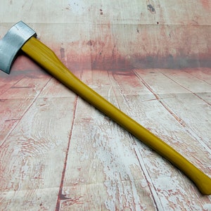 May include: A silver axe with a yellow wooden handle. The axe is lying on a wooden surface.