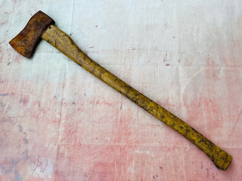 K&ouml;nnte beinhalten: Eine antike Axt mit einem Holzstiel. Die Axtkopf ist rostig und der Stiel ist vom Alter vergilbt.