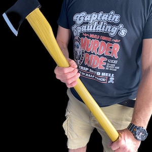 K&ouml;nnte beinhalten: Eine Person h&auml;lt eine Axt mit schwarzem Griff und einem Holzstiel. Die Axt wird in bedrohlicher Weise gehalten. Die Person tr&auml;gt ein schwarzes T-Shirt mit dem Aufdruck "Captain Spaulding's World Famous Murder Ride". Der Text "See! Ed Gein, Elbert Fish, Dr. Satan Trip Into Hell 1/2 Price!" ist ebenfalls auf dem Shirt aufgedruckt.