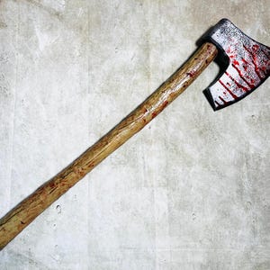 May include: An axe with a wooden handle and a metal head stained with red paint, resembling blood.