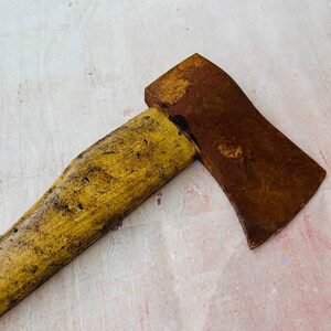 K&ouml;nnte beinhalten: Eine rostige Axt mit einem gelben Holzstiel. Der Axtkopf ist braun und leicht gebogen.