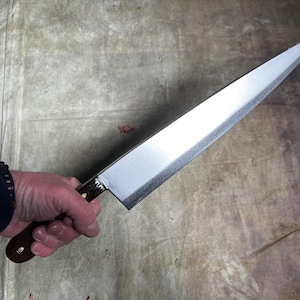 May include: A long, silver kitchen knife with a wooden handle. The knife is held in a hand, with the blade pointing towards the right.