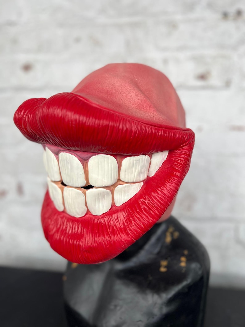 Puede incluir: Una m&aacute;scara de pl&aacute;stico roja y blanca con una gran sonrisa de dientes y labios exagerados. La m&aacute;scara est&aacute; dise&ntilde;ada para parecerse a la boca de una persona.