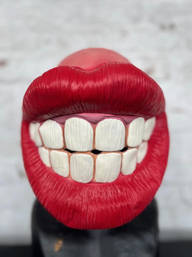 Puede incluir: Una boca grande de pl&aacute;stico rojo con dientes blancos sonr&iacute;e ampliamente. La boca es un art&iacute;culo novedoso y podr&iacute;a usarse como accesorio o decoraci&oacute;n.