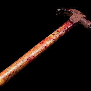 Pu&ograve; includere: Un martello insanguinato con un manico di legno. Il martello &egrave; arrugginito e presenta schizzi di sangue rosso sul manico.