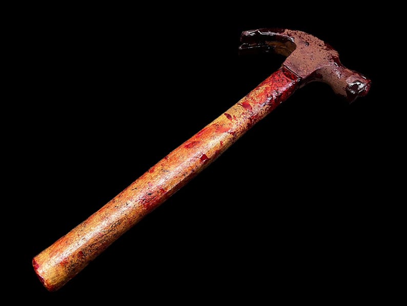 Pu&ograve; includere: Un martello insanguinato con un manico di legno. Il martello &egrave; arrugginito e presenta schizzi di sangue rosso sul manico.