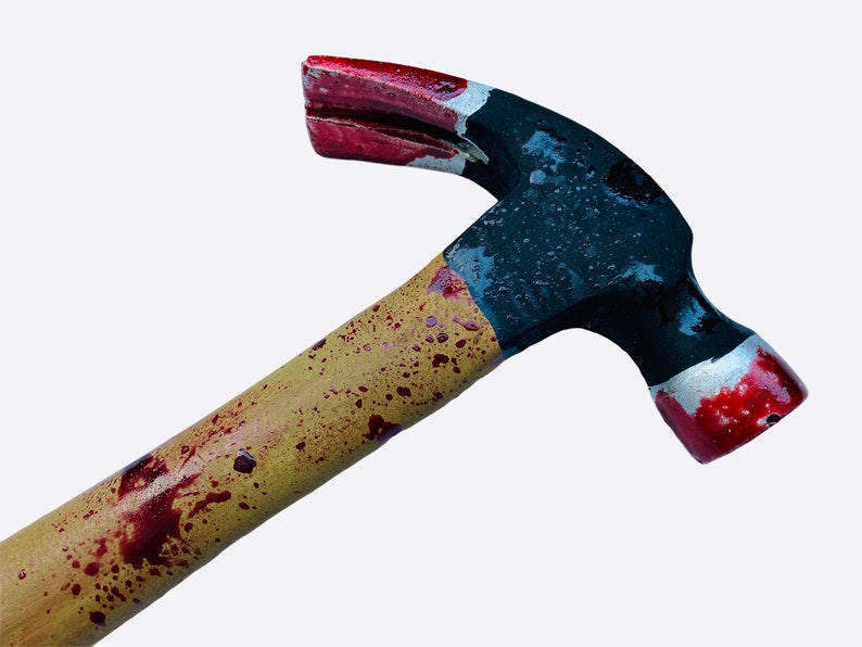 May include: A black and red hammer with a wooden handle stained with red splatter paint. The hammer has a claw on the back.