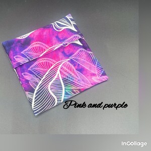 Puede incluir: Una bolsa de tela rosa y morada con un patrón de hojas blancas. La bolsa está doblada por la mitad y tiene una costura blanca en el centro.