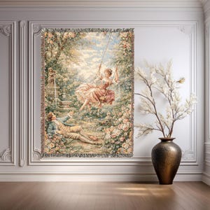 May include: Woven tapestry depicting a romantic garden scene with a woman on a swing and a man reclining. The tapestry, with a fringed edge, uses pink, green, and beige tones. It is displayed on a white wall, creating a classic aesthetic.