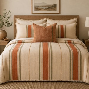 May include: A bed with a cream-colored comforter and matching pillow shams. The comforter and shams have vertical stripes in shades of orange and green. A textured orange pillow sits in the center. The bed is made up with a wooden headboard.