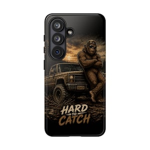 Könnte beinhalten: Schwarze Handyhülle mit einer braunen Bigfoot-Illustration, die sich an einen braunen Pickup-Truck lehnt. Der Text "HARD TO CATCH" ist goldfarben. Der Hintergrund zeigt einen Sonnenuntergang.