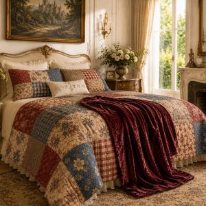 May include: A bed with a patchwork quilt in shades of red, blue, and beige. The quilt features floral and plaid patterns. Matching throw pillows and a burgundy throw blanket complete the bedding set. The room has a classic, elegant style.