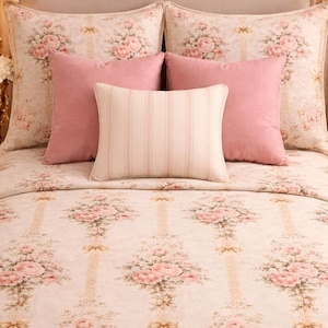 Puede incluir: Una cama con una colcha y fundas de almohada estampadas con flores. La ropa de cama presenta un patrón repetido de rosas rosas y lazos sobre un fondo crema. Tres almohadas rosas y una almohada a rayas están en la cama.