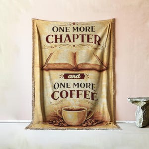 Könnte beinhalten: Eine beige Decke mit dem Text "ONE MORE CHAPTER and ONE MORE COFFEE". Das Design umfasst ein offenes Buch, eine Kaffeetasse und Kaffeebohnen. Die Decke hat einen Fransenrand.