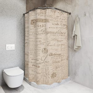 May include: A beige shower curtain with a vintage script design, featuring French text and stamps. The curtain hangs in a bathroom with a white toilet and a towel. The shower curtain is suspended from a curved metal rod.