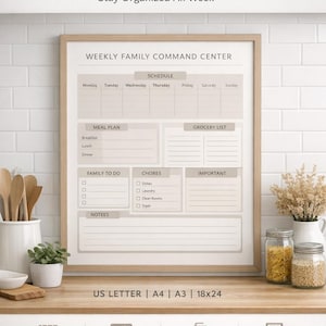 May include: A framed weekly family command centre in neutral tones. The schedule includes sections for meal planning, grocery lists, chores, and notes. The frame is displayed on a wooden surface with decorative elements.