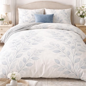 May include: A bed with a white duvet cover and matching pillowcases, adorned with a delicate blue leaf pattern. A blue decorative pillow rests on top. The bed is flanked by nightstands with lamps and a tray with cups.