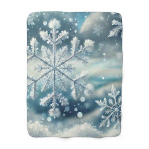 May include: A rectangular blanket with a winter theme, showcasing large, detailed snowflakes in white and light blue hues. The design creates a snowy, dreamy ambiance, with a soft, blurred background.