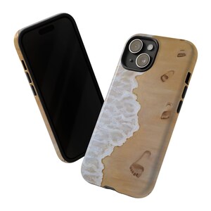 Puede incluir: Una funda de teléfono negra con un diseño de playa. La funda presenta una ola blanca rompiendo en una playa de arena con huellas en la arena.