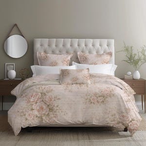 May include: A bed dressed with a floral duvet cover and pillow set. The bedding displays large pink roses on a cream backdrop. The headboard is upholstered in a light beige fabric. Two bedside tables with decor flank the bed.