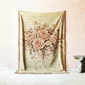 Peut inclure: Une couverture beige avec un grand bouquet floral de roses roses et de petites fleurs blanches attachées avec un ruban. Le fond présente une écriture manuscrite. La couverture a un bord à franges.