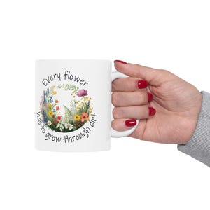 Puede incluir: Taza de cerámica blanca con un diseño floral y el texto "Every flower has to grow through dirt".
