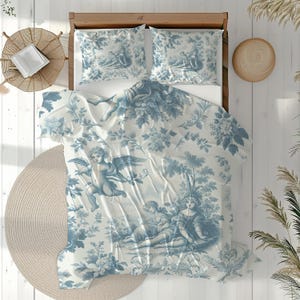 Puede incluir: Un juego de cama de toile de Jouy azul y blanco con una escena pastoral detallada con querubines, motivos florales y follaje. El juego incluye una funda n&oacute;rdica y dos fundas de almohada. La ropa de cama est&aacute; colocada sobre una estructura de cama de madera.