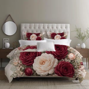 May include: A bed with a floral duvet cover and pillow set. The duvet features large, burgundy and cream-colored roses with green foliage. White pillows and a tufted headboard complete the bedding ensemble. A round mirror hangs on the wall.