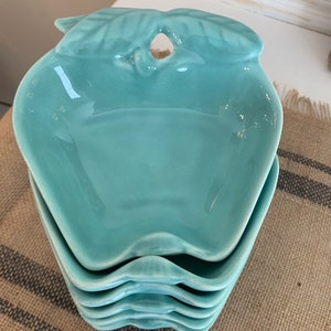 May include: Set of four teal blue ceramic apple-shaped bowls. The bowls are stacked on top of each other.