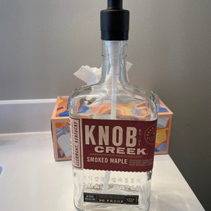 May include: A clear glass bottle repurposed as a soap dispenser, featuring a black pump and the "Knob Creek" label. The label is brown and red with the words "Smoked Maple" and "90 Proof".