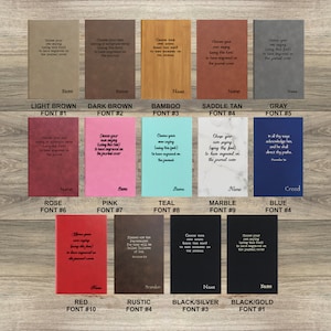May include: A chart showing ten different leather-bound journals with various colors and fonts. The colors include light brown, dark brown, bamboo, saddle tan, gray, rose, pink, teal, marble, blue, red, rustic, black/silver, and black/gold. The fonts are numbered 1 through 10. The text on the journals says "Choose your own saying or scripture verse (using this font) to have engraved on the journal cover."