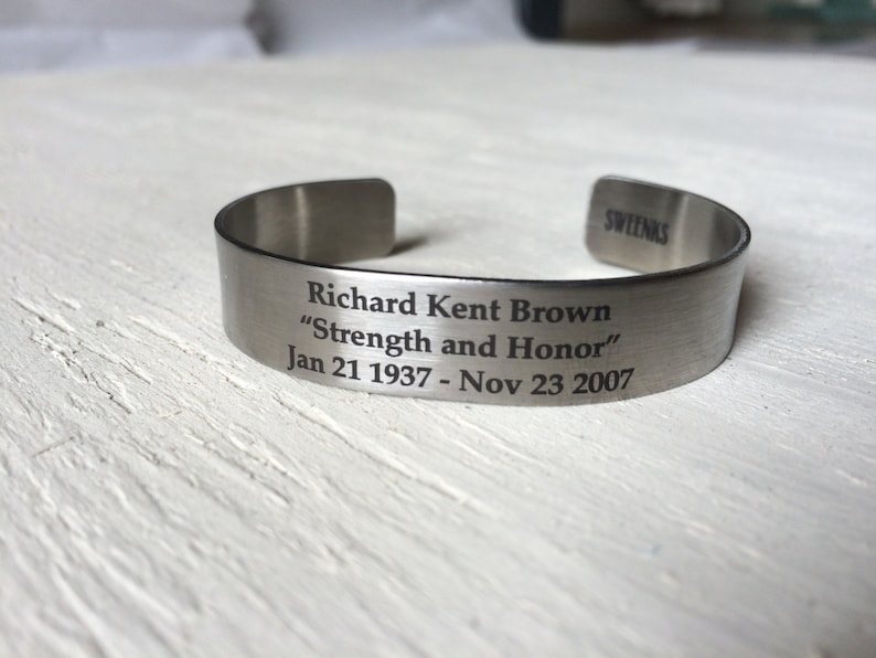 May include: A silver metal bracelet engraved with the words "Richard Kent Brown", "Strength and Honor", and the dates "Jan 21 1937 - Nov 23 2007".