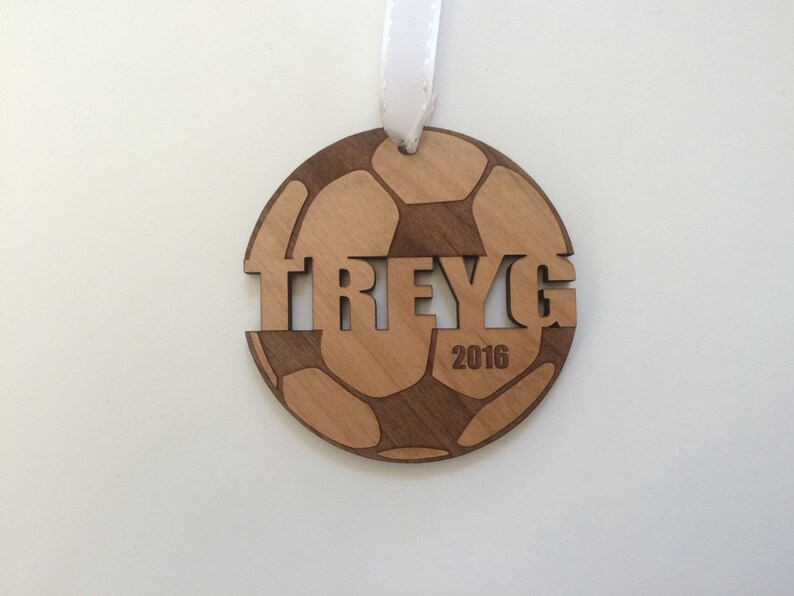 May include: A wooden soccer ball ornament with the name "TREY" and the year "2016" engraved on it.