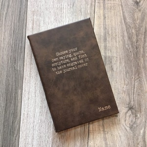 May include: A brown leather journal with the text "Choose your own saying, quote, scripture, and font to have engraved on the journal cover" and the word "Name" printed on the cover.