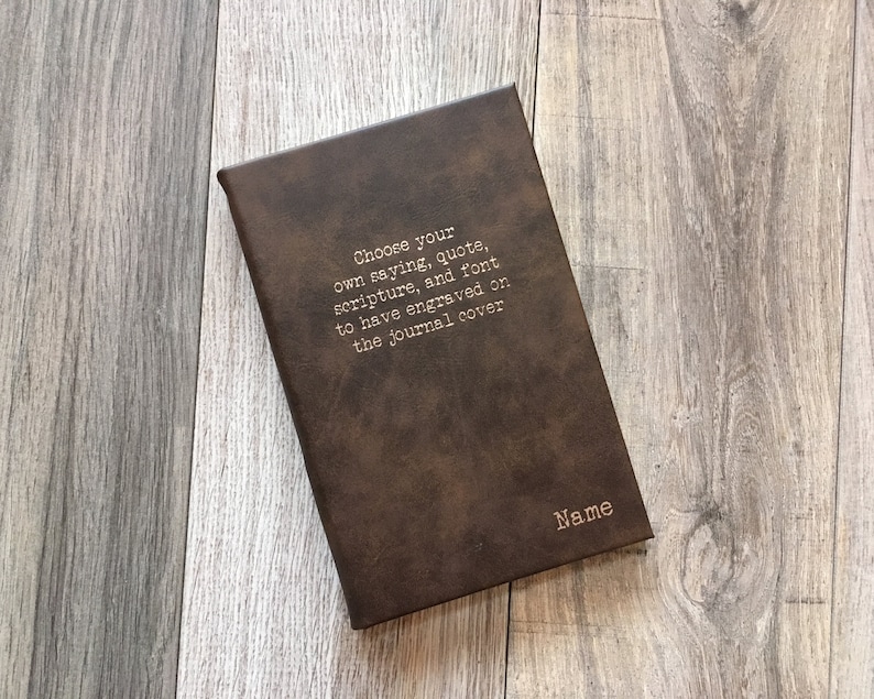 May include: A brown leather journal with the text "Choose your own saying, quote, scripture, and font to have engraved on the journal cover" and the word "Name" printed on the cover.