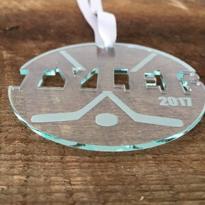 Pu&ograve; includere: Un ornamento da hockey in vetro trasparente con la parola "Yzer" e l'anno "2017" incisi su di esso.