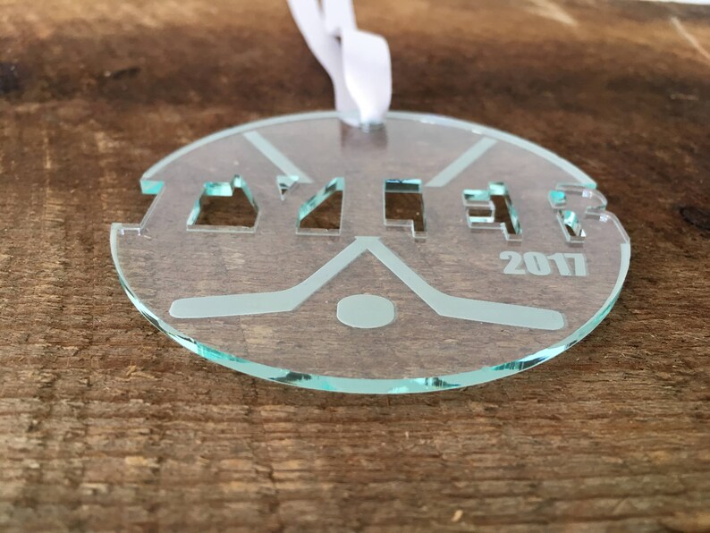 Pu&ograve; includere: Un ornamento da hockey in vetro trasparente con la parola "Yzer" e l'anno "2017" incisi su di esso.