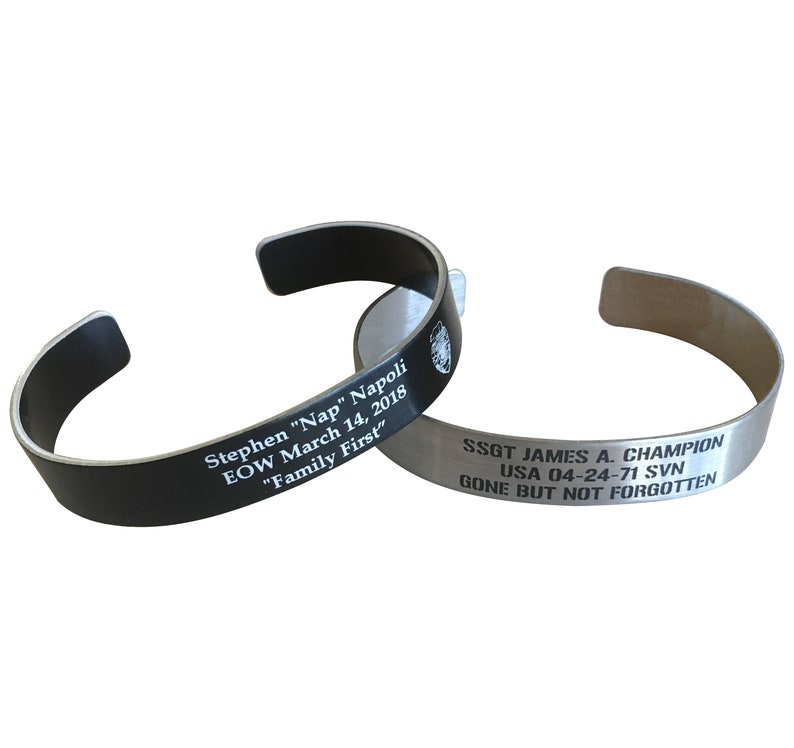 May include: Two engraved metal bracelets. The black bracelet reads "Stephen "Nap" Napoli EOW March 14, 2018 "Family First". The silver bracelet reads "SSGT JAMES A. CHAMPION USA 04-24-71 SVN GONE BUT NOT FORGOTTEN".