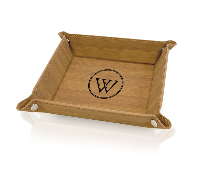May include: A square bamboo valet tray with a light brown finish. The tray features a stitched leather border and metal snap closures at each corner. A black circular emblem with the letter "W" is centered on the tray's base.