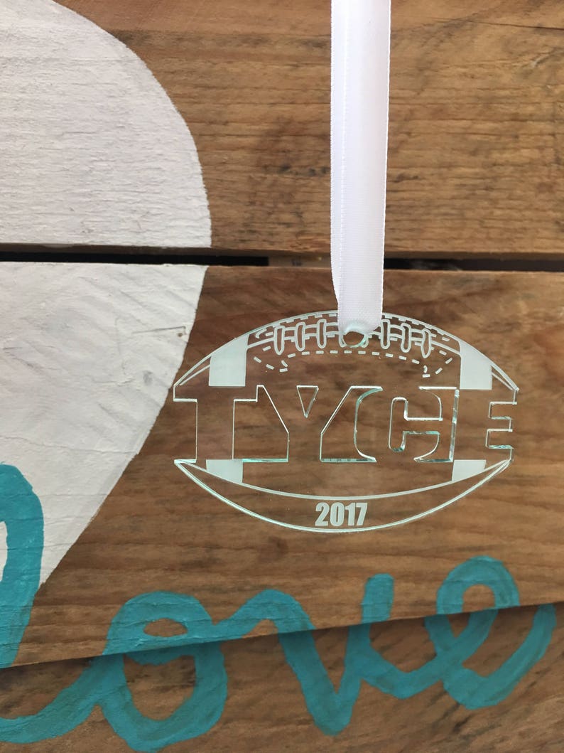 Pu&ograve; includere: Un ornamento da albero di Natale a forma di pallone da calcio in acrilico bianco con il nome "Tyce" e l'anno "2017" incisi su di esso. L'ornamento &egrave; appeso a un nastro bianco.