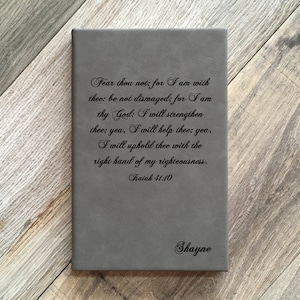 May include: A gray leather journal with the text "Fear thou not; for I am with thee: be not dismayed; for I am thy God: I will strengthen thee; yea, I will help thee; yea, I will uphold thee with the right hand of my righteousness. Isaiah 41:10" and the name "Shayne" printed on the front.