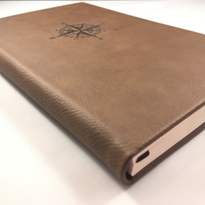 May include: A brown leather-bound journal with a compass design and the word "Journal" embossed on the cover.